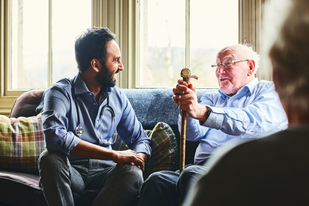 Smiling doctor visiting with senior man on couch